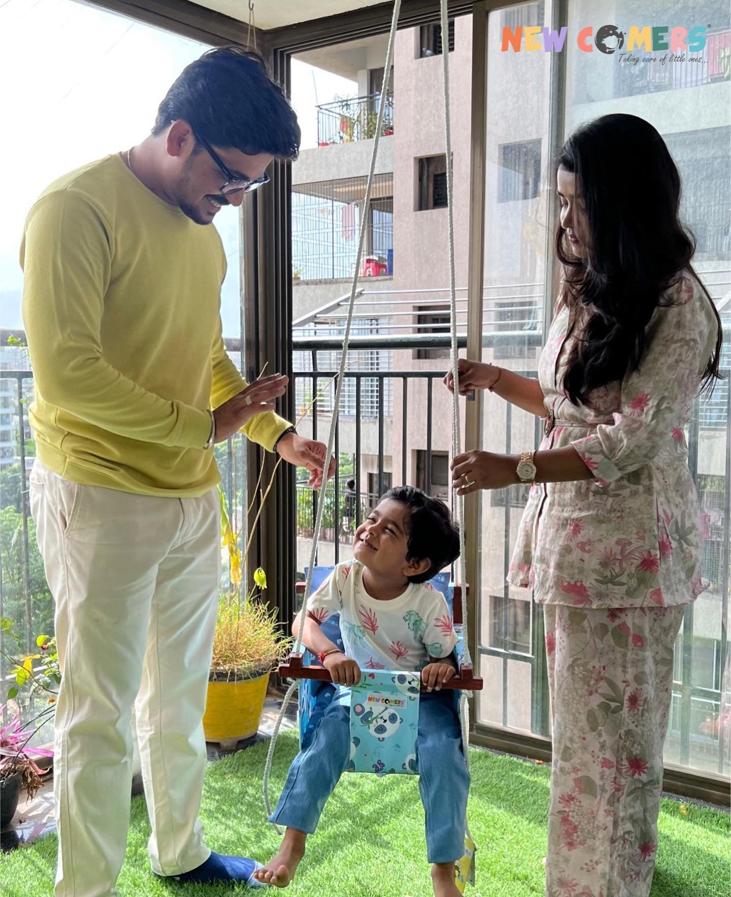 a couple with their kid in blue baby jhula in their balcony enjoying their happy swing time by newcomers