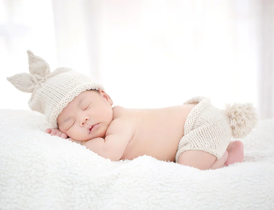 cute baby with woolen hat sleeping of a furry white bed on his tummy