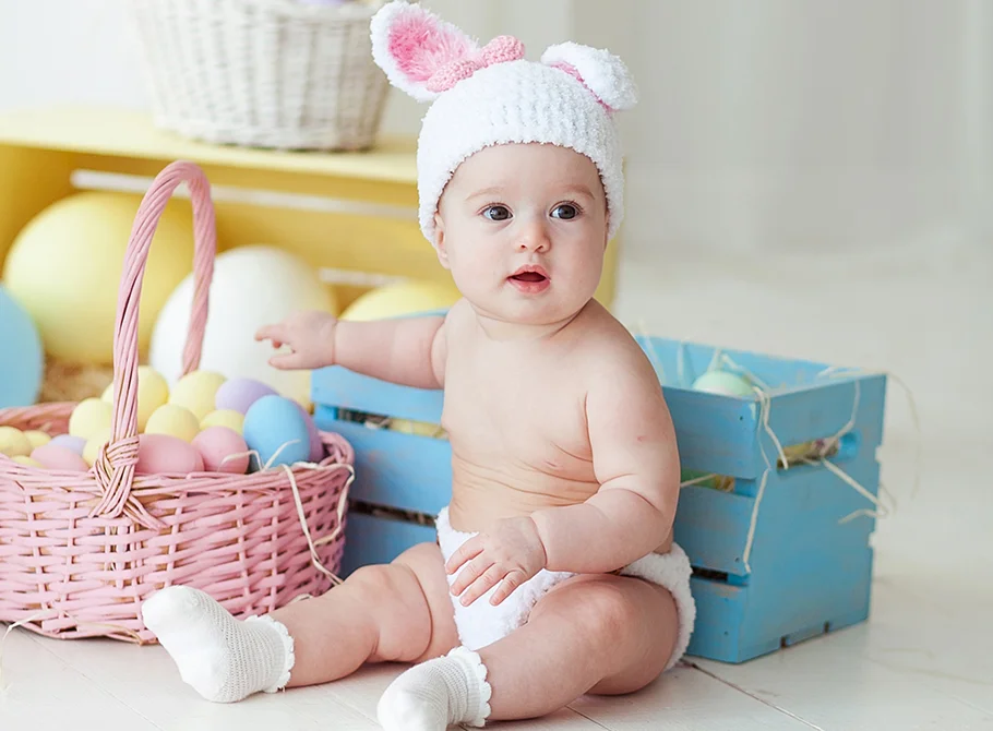 a cute girl wearing woolen rabbit hat sitting near basket full of colorful eggs