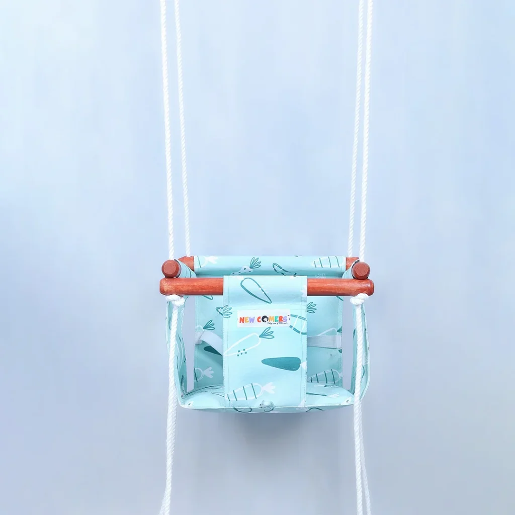 bright baby blue colored small size jhula for kids hanging with ropes passing through 4 wooden frames, this Bucket swing for 6 month old with carrot prints of NEWCOMERS brand