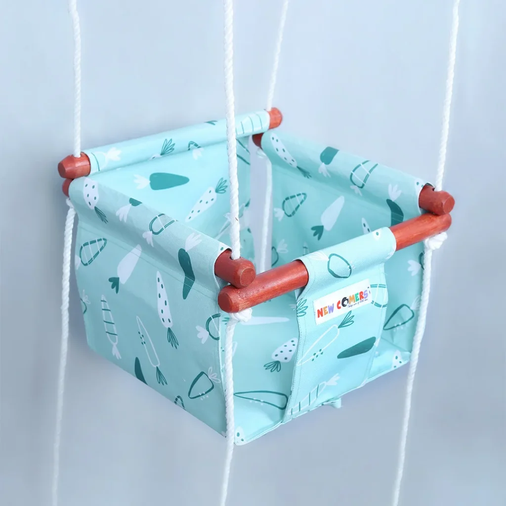 bright baby blue colored small size jhula for kids hanging with ropes passing through 4 wooden frames, this Bucket swing for 6 month old with carrot prints of NEWCOMERS brand