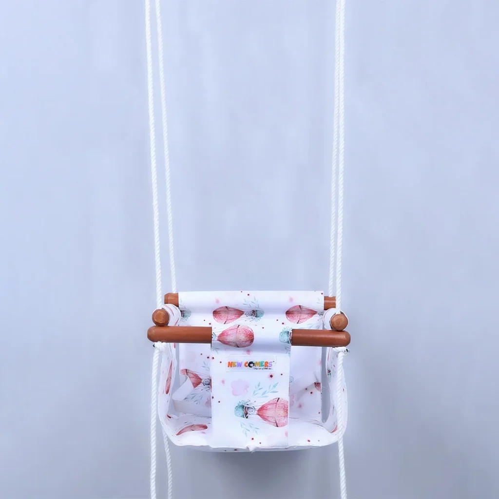 white fabric jhula for babies with small parachute prints, hanging with four ropes passings through wooden jhula frames