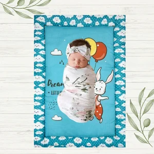 blue fabric rabbit in jumpsuit flying using 3 balloons saying "dream big, little one" newborn mat with baby sleeping peacefully on it made by newcomers